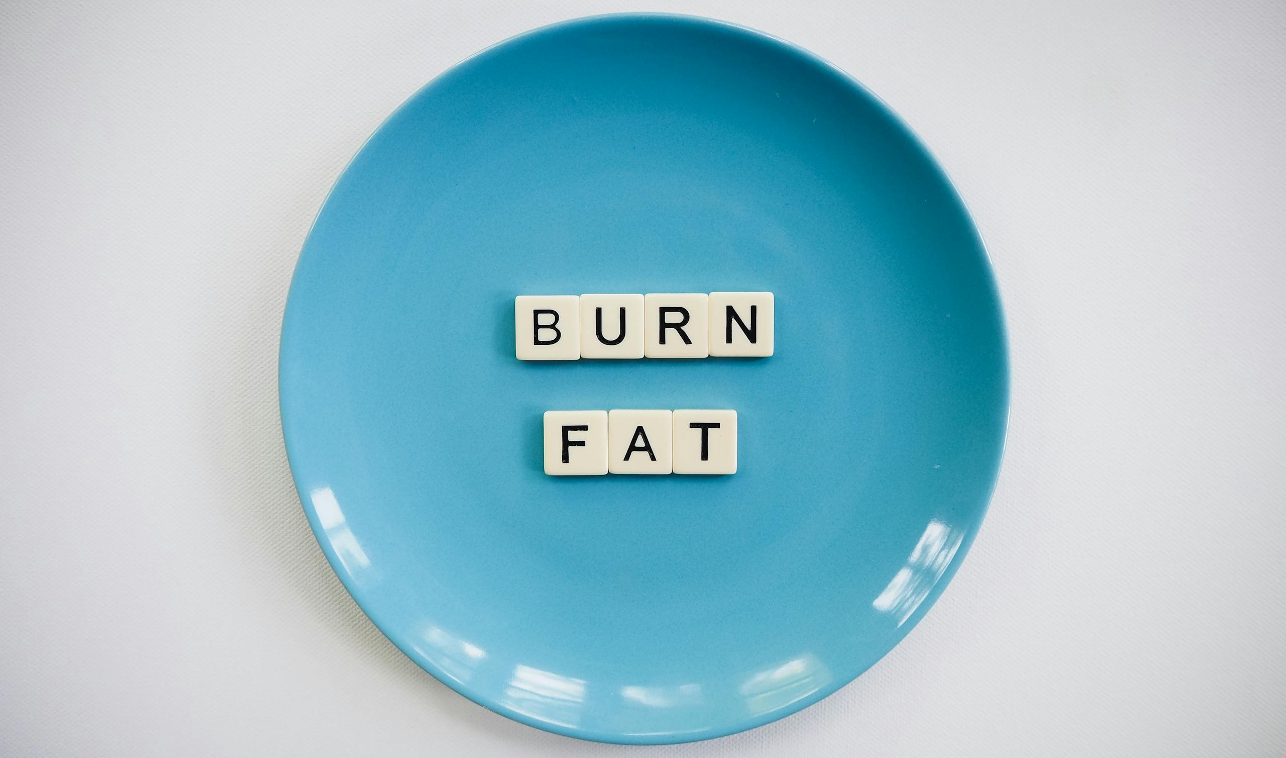 A conceptual image featuring the words 'Burn Fat' on a blue plate, symbolizing weight loss.